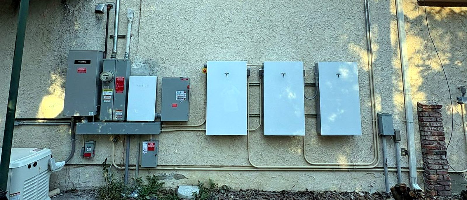 Three Tesla Powerwall batteries beside a standby generator, installed by Current Energy