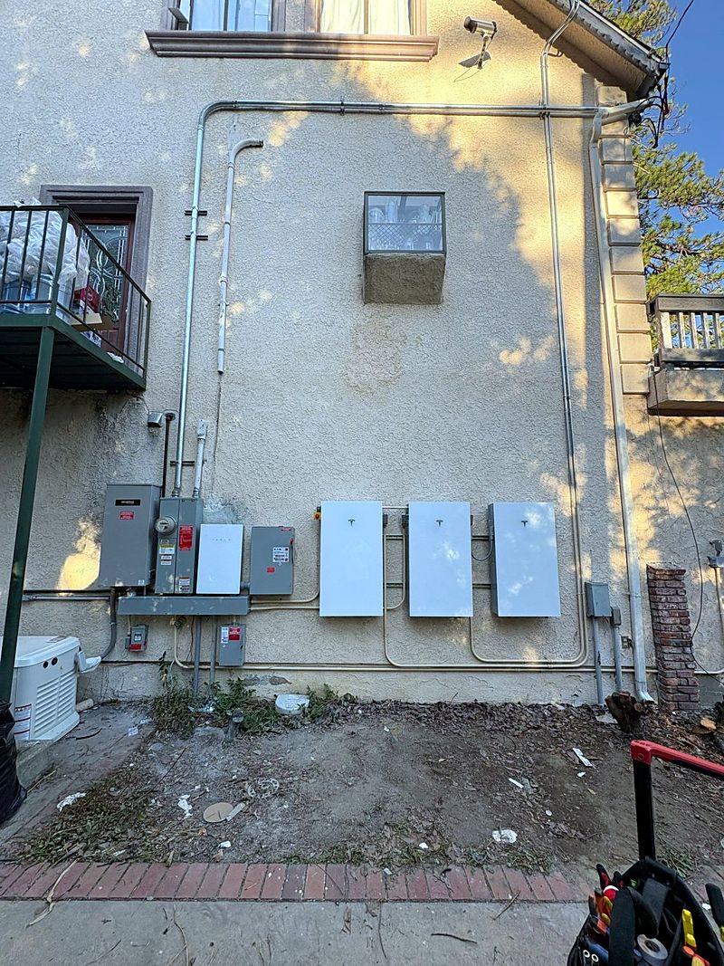 Three Tesla Powerwall batteries beside a standby generator on a home
